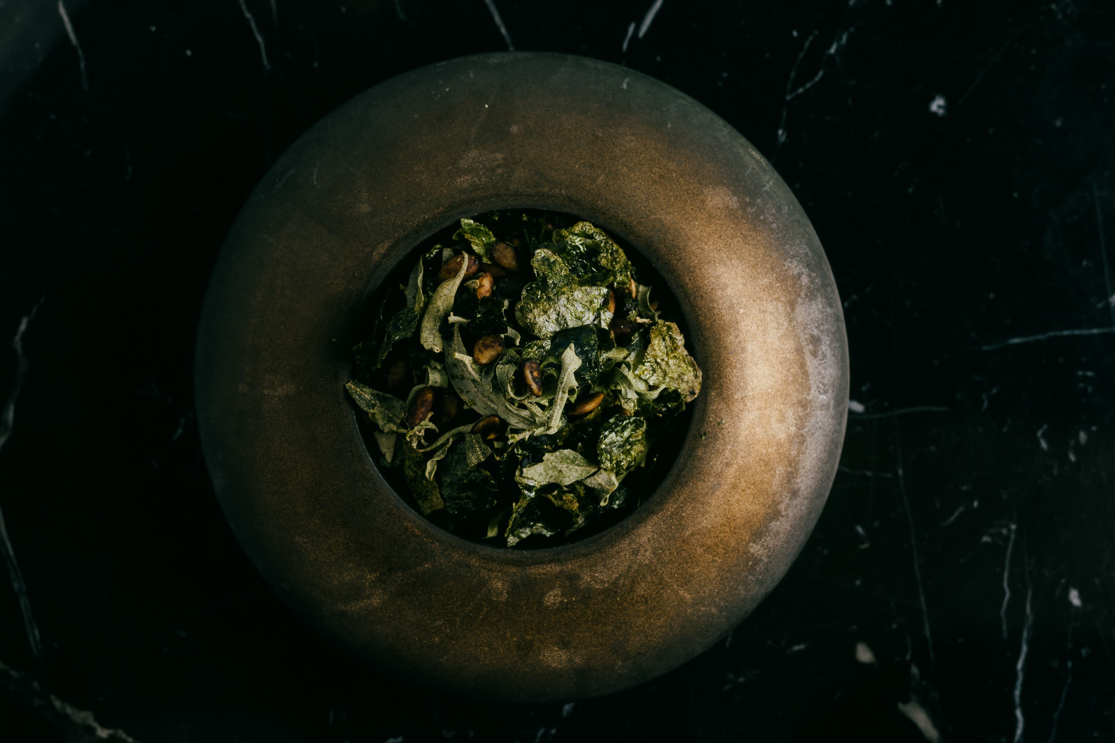 A dimly lit gold toned bowl with cripsy charred green vegetables