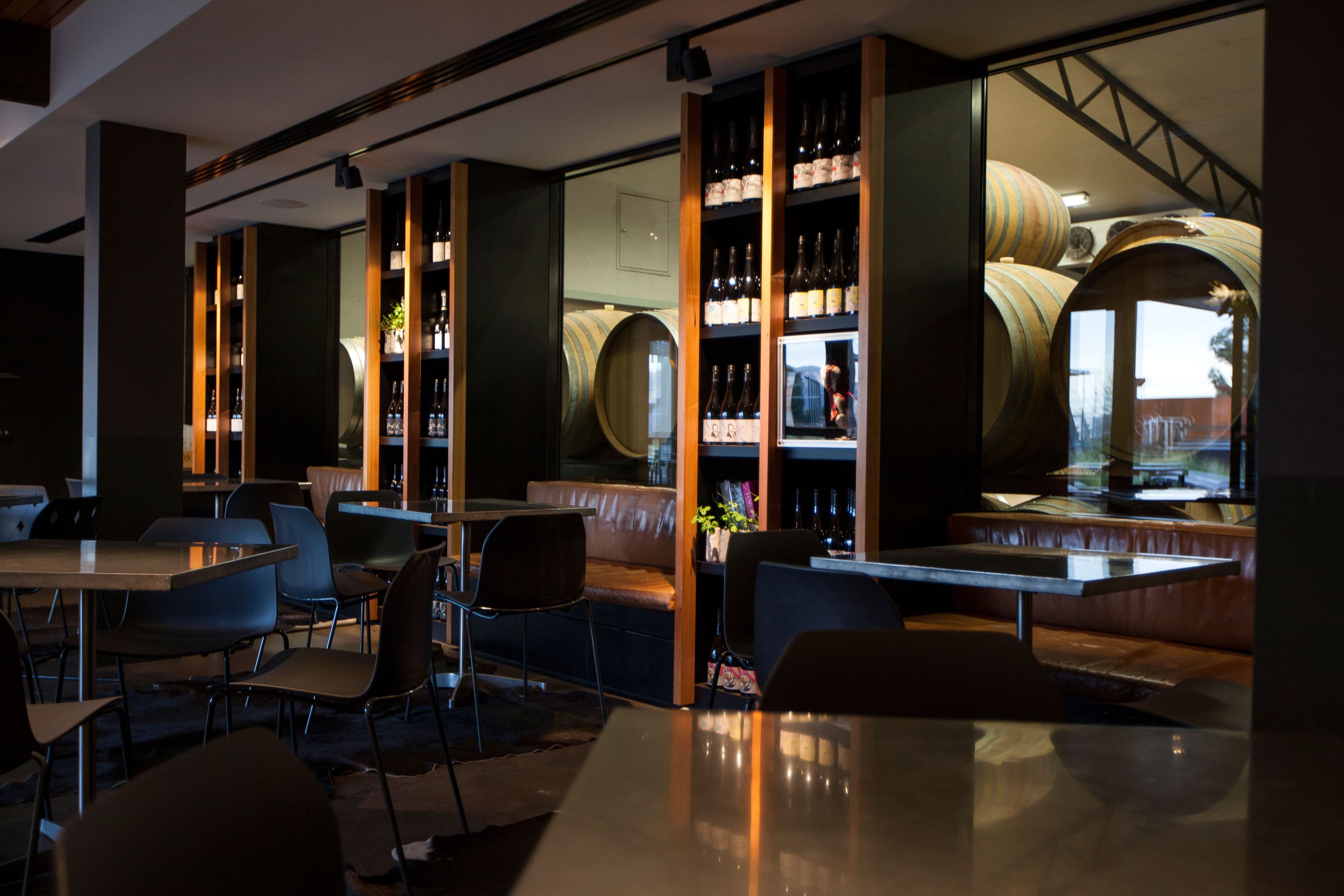 Internal image of the Wine Bar with leather bench seats, metal tables and wine barrells through the glass of the room next door