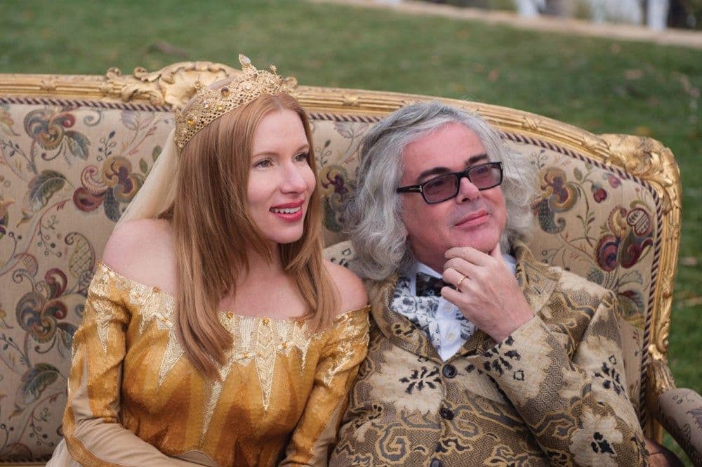 Kirsha and David in their wedding attire seated side by side on a couch of gold and embroidery