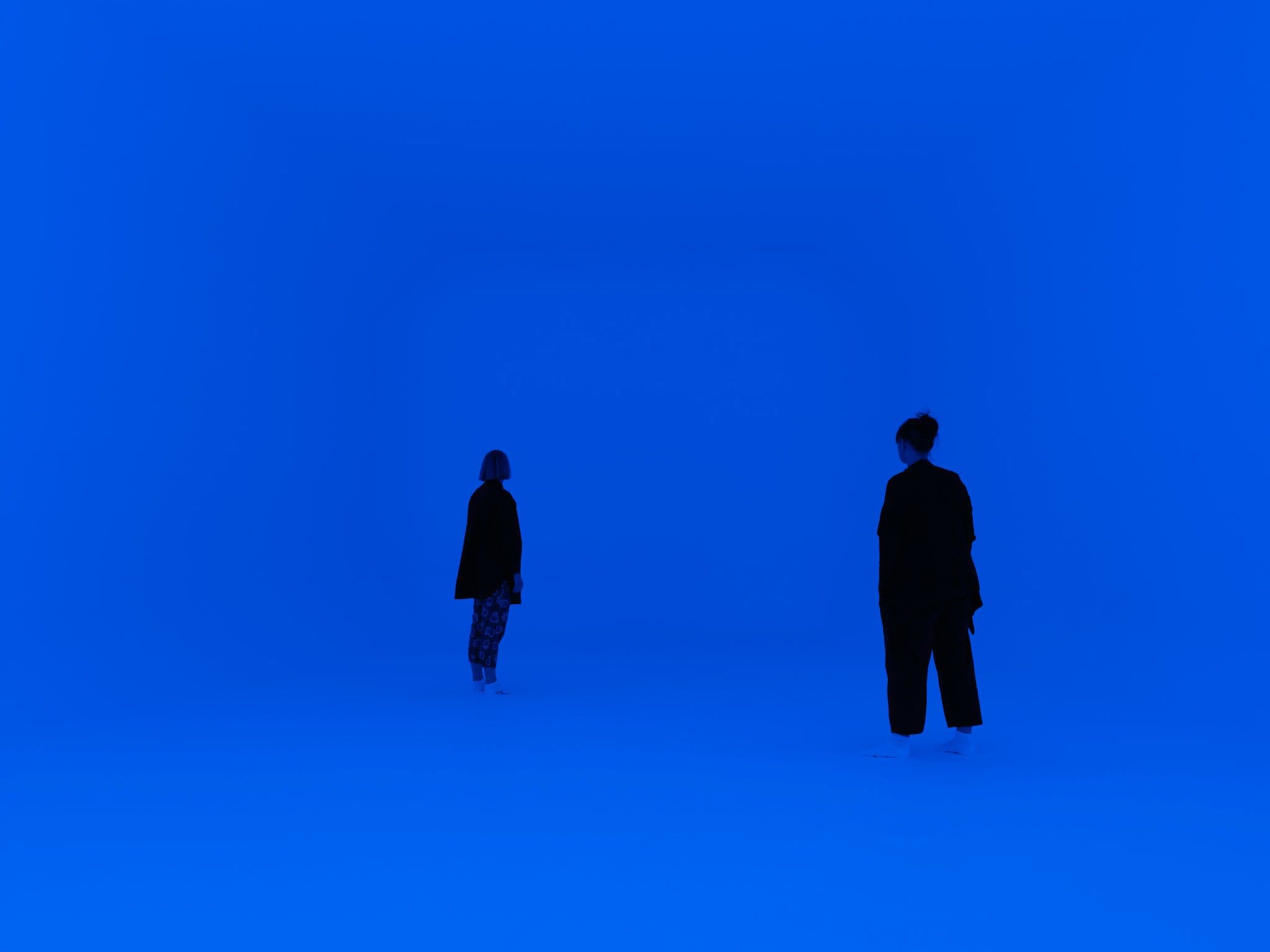 Two figures in a room lit in hues of blue.