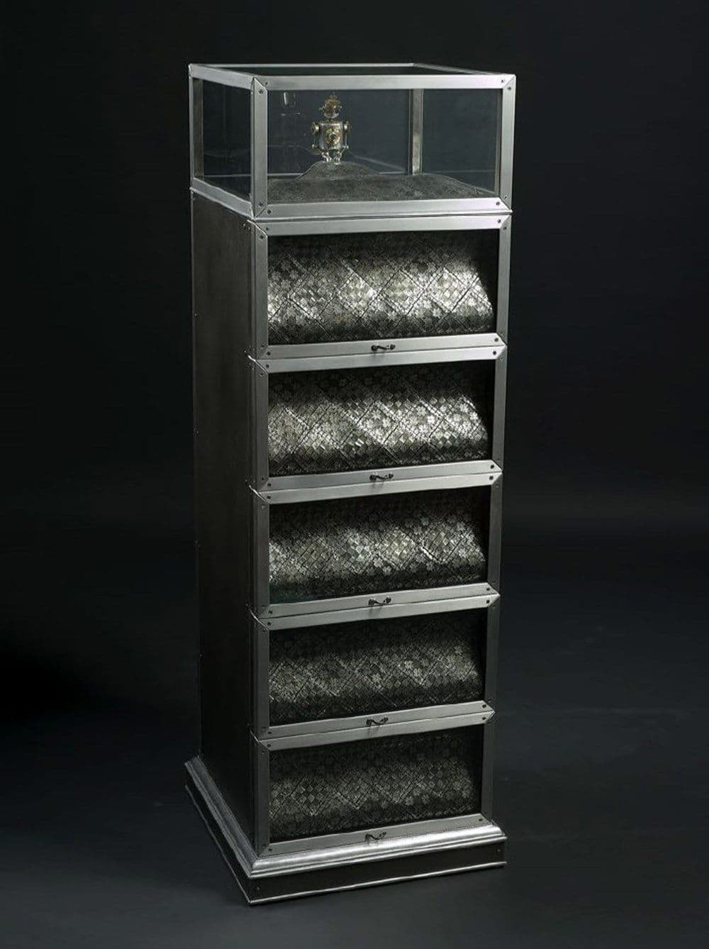 A silver tower with silver tapestry like pieces stored underneath a glass top