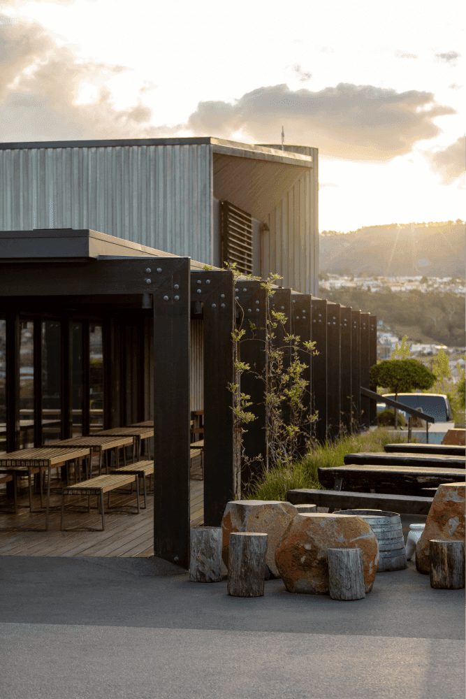 Sun sets over empty wine bar outdoor seating (wooden tables, wine barrel seats)