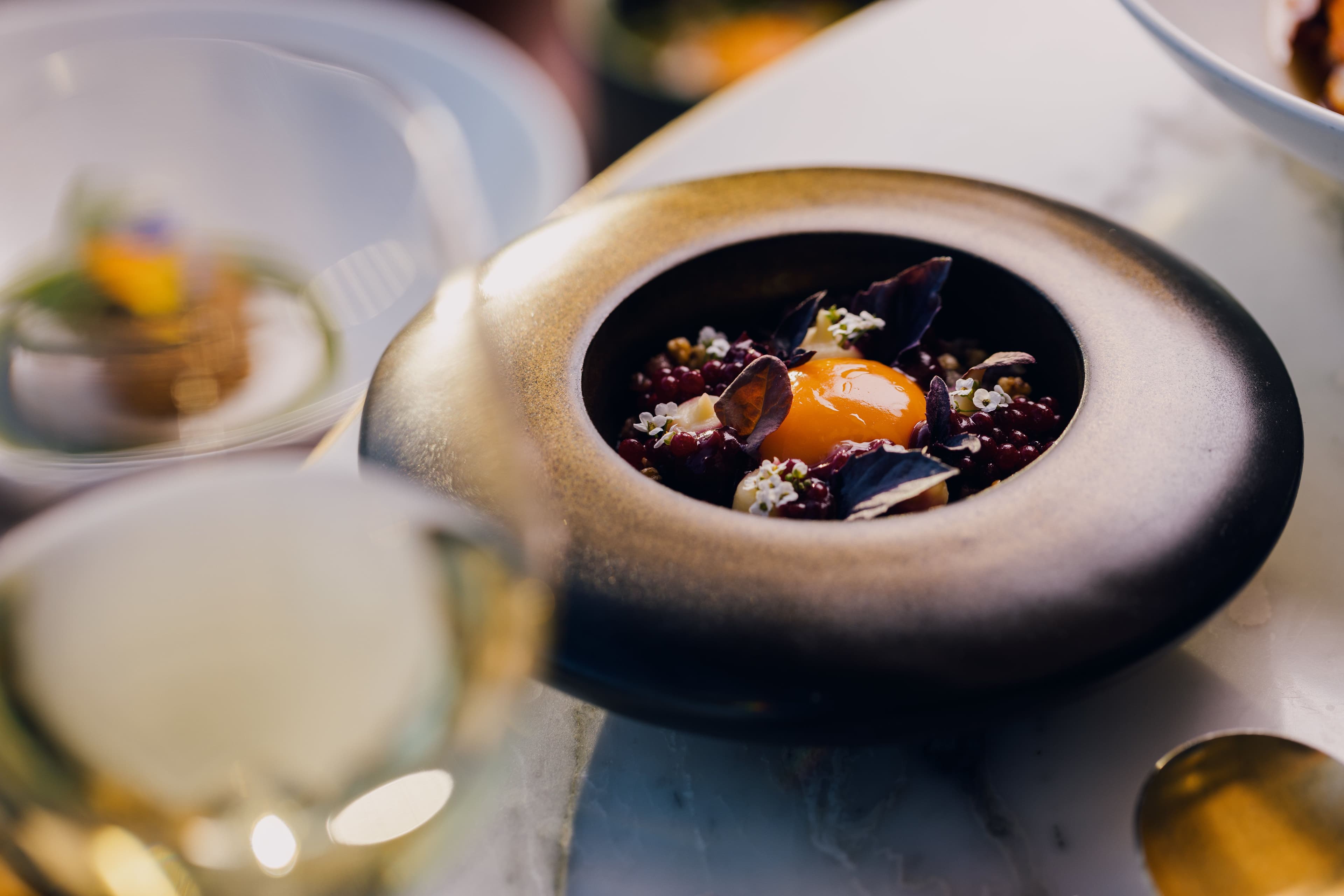 An unusual shaped ceramic containing a dish of egg yolk garnished with dark leaves